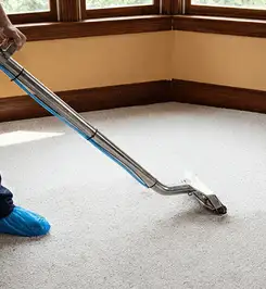 Steam carpet cleaning technician using a hot-water extraction wand on a residential carpet, wearing blue protective shoe covers Fort Collins, CO.