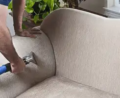 Professional upholstery cleaner deep-cleaning a fabric sofa with a handheld extraction tool and hose in Fort Collins, CO.